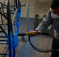 A person powder-coating metal brackets wearing safety gear