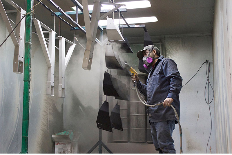 A person powder-coating metal brackets wearing safety gear